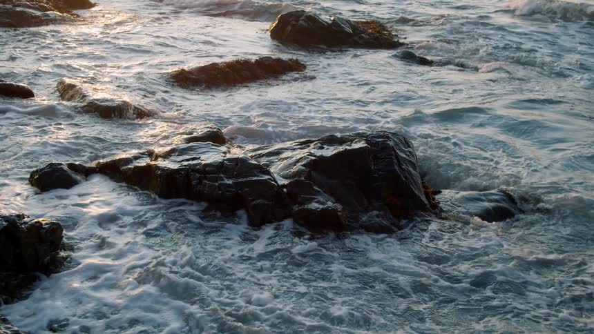 Ocean waves crash on the rocks in the coast at sunset
