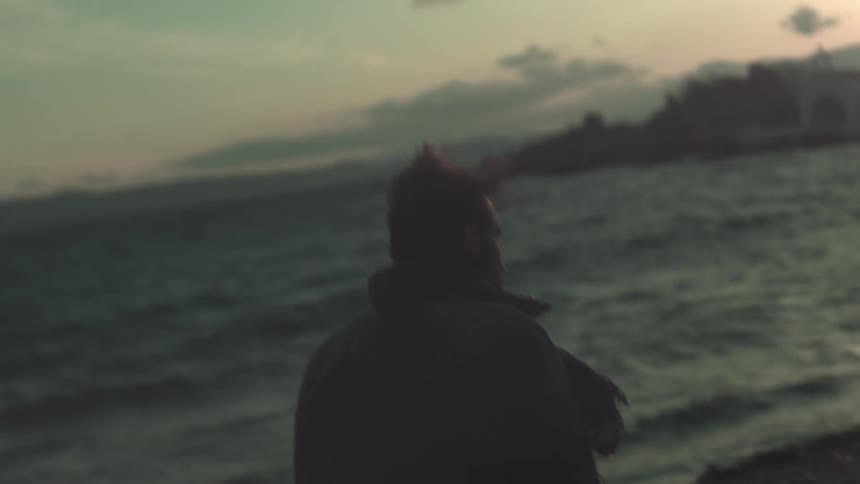 A man walking along the shoreline while waves crash and the wind is strong