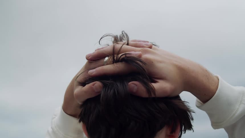 A young man holds his hands on his head, looking over the skyline.