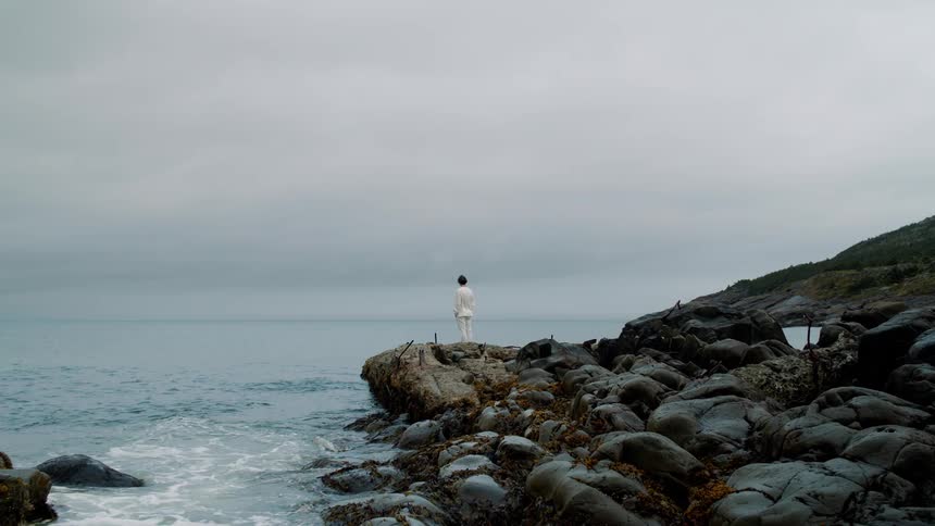 A person stands along a coastal rock formation looking towards the ocean water