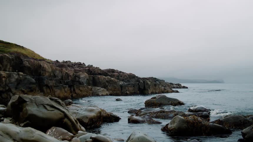 Sea waves crash on the rocks of a coast on an overcast day