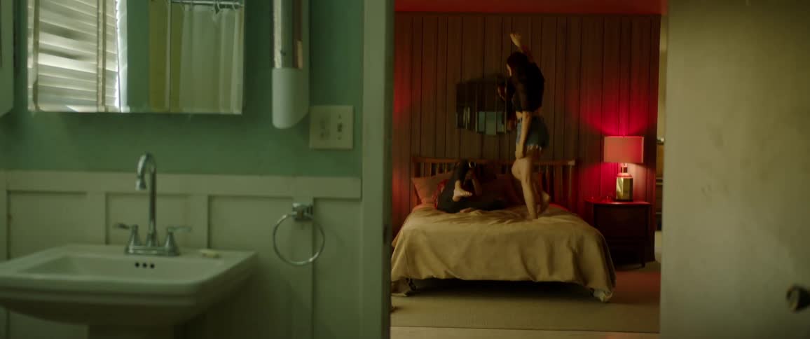 A young woman jumps on a hotel bed while a man films her
