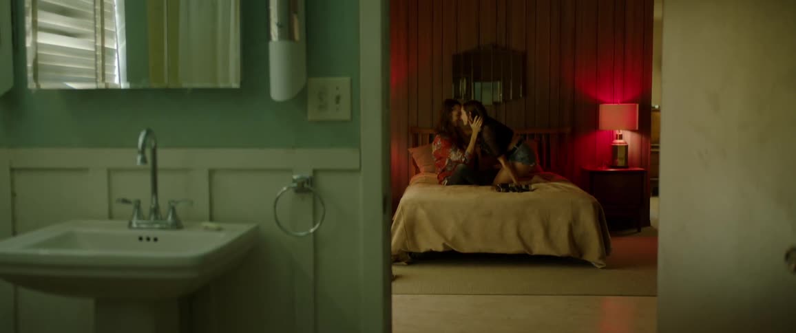 Two teenagers sitting on a motel bed playfully kissing