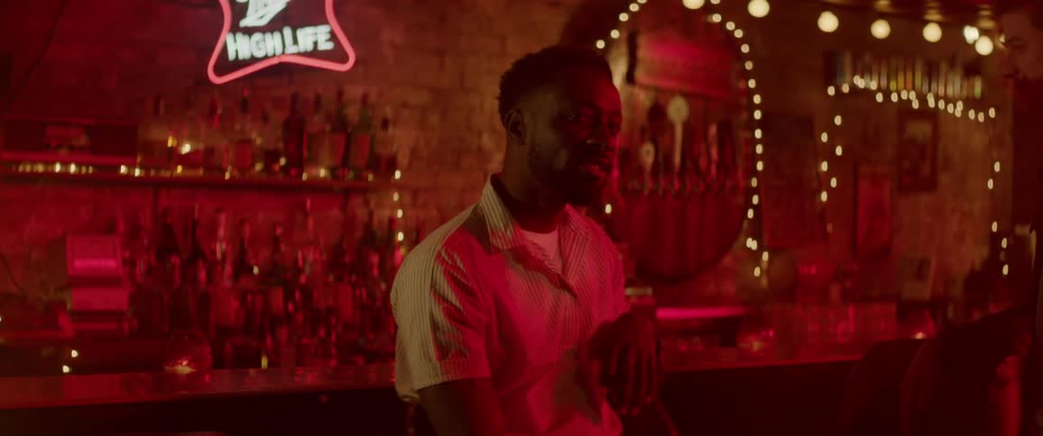 A man at a bar smiling, laughing and looking towards the dance floor