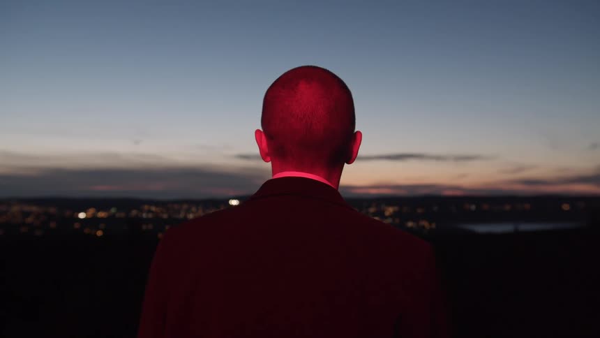 A man stands and looks at the city skyline lit up at night