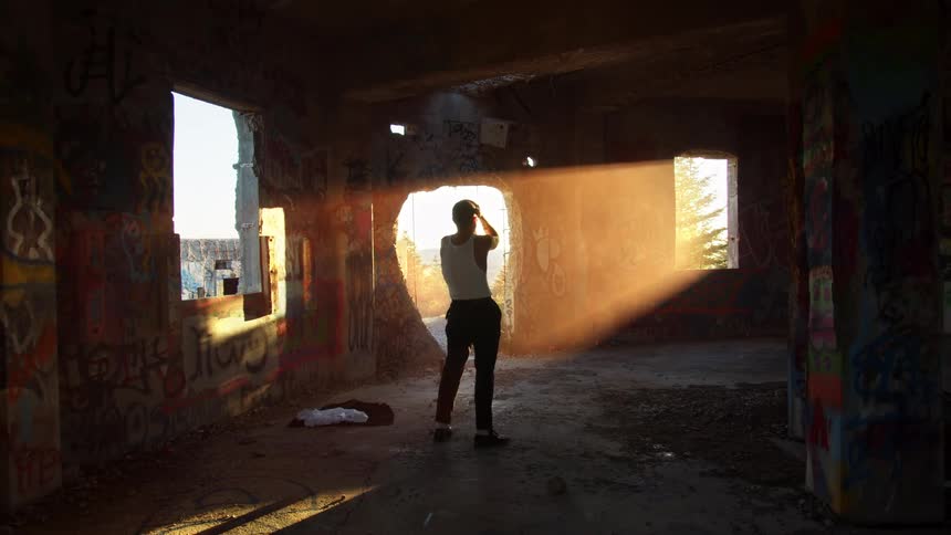A person in a room with graffiti standing as sunlight shines through a window