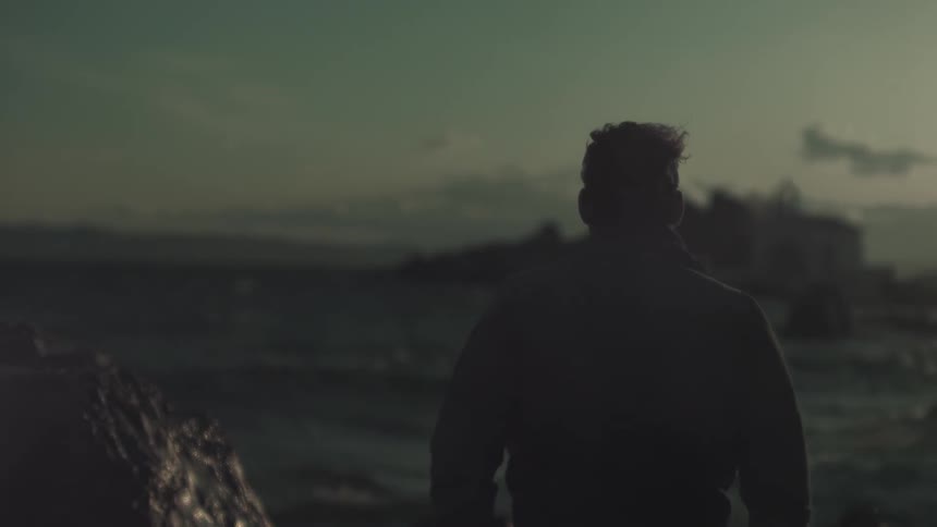 A man looks out towards the ocean at dusk
