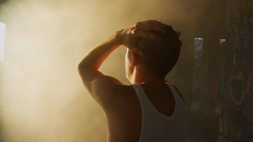 Man in an undershirt rubs his hands over his head while standing outdoors
