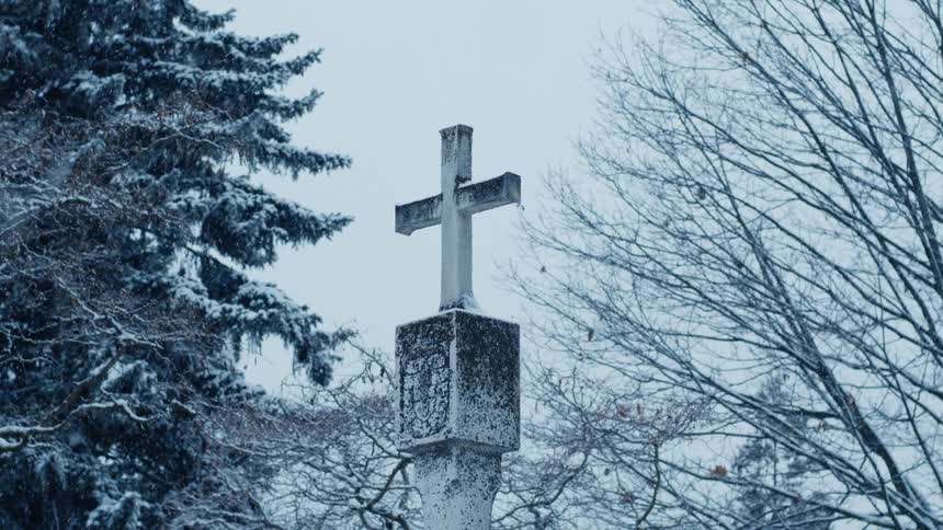 Snow falls on a cross on the top of a church