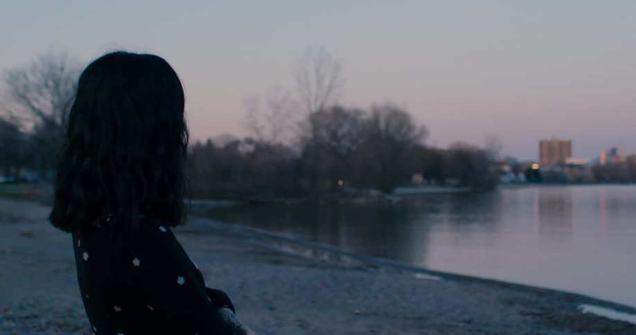 Woman in a black dress stands in the shoreline of a lake at sunset