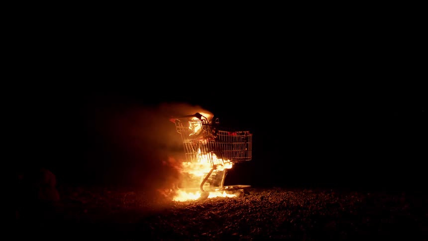 A shopping burns on fire on a rocky beach at night