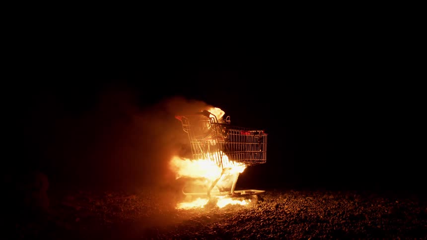 A shopping burns on fire on a rocky beach at night