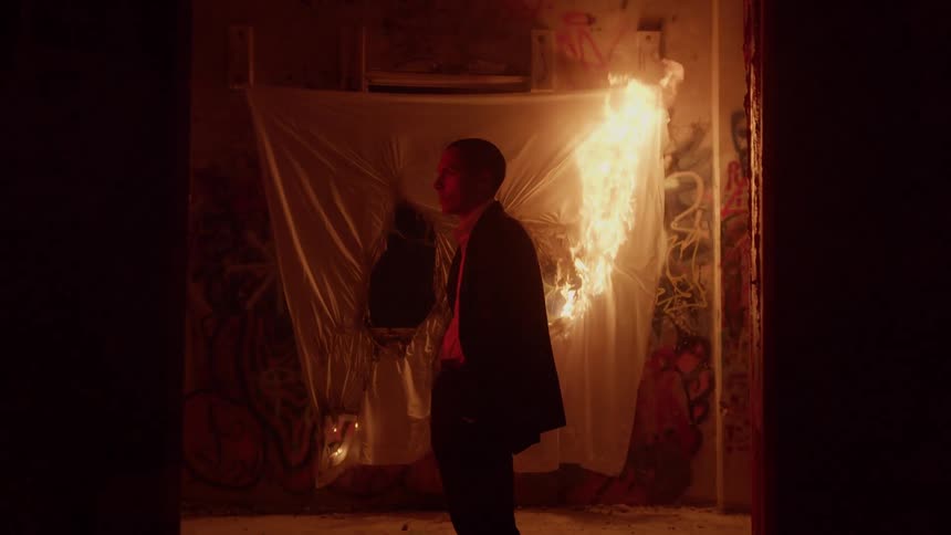 A young man stands in front of a sheet during on a wall in an abandoned building