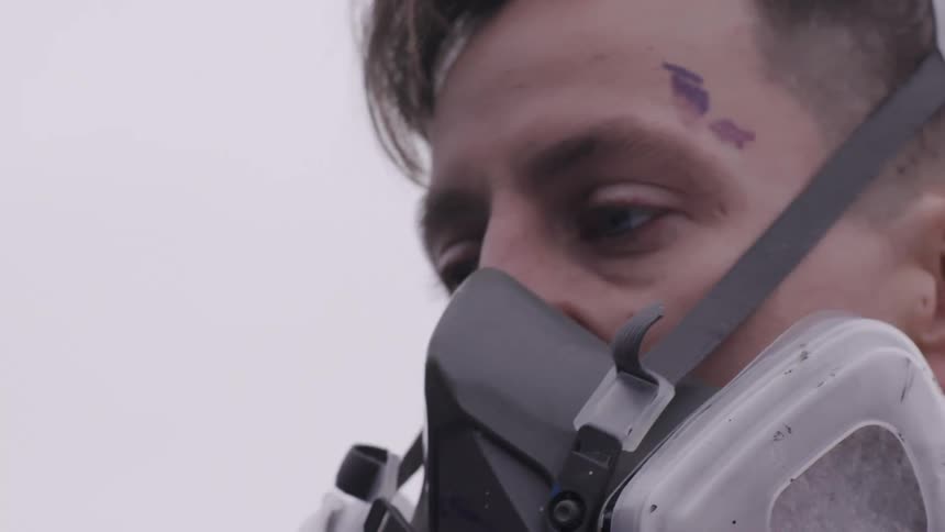 Man wearing a respirator face mask spray paints a graffiti on a wall outside