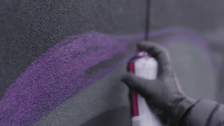 Man wearing gloves sprays a graffiti on a wall