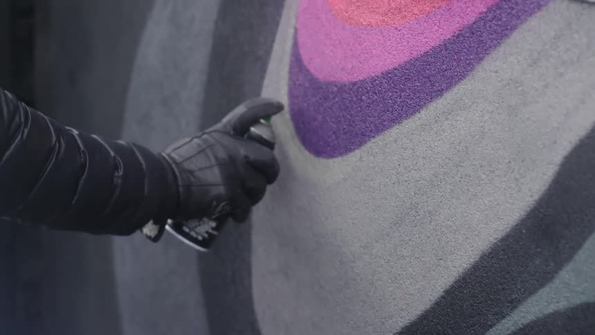 Person wearing black gloves uses a spray can to paint a graffiti on a wall