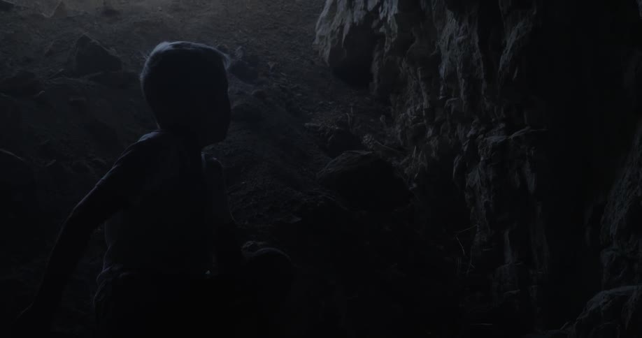 A young boy sits at the base of a darkened and rocky dirt path
