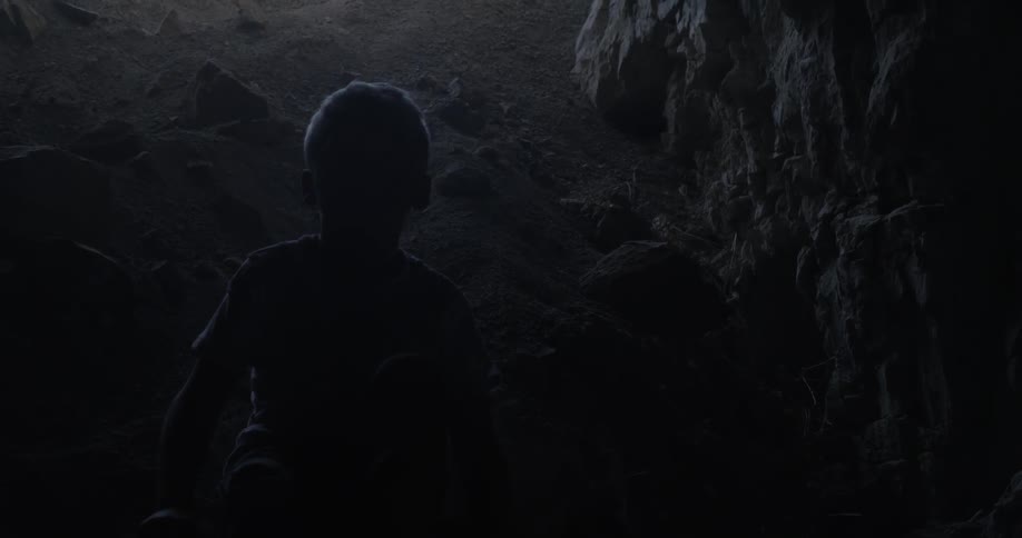 A boy is standing in a dark cave