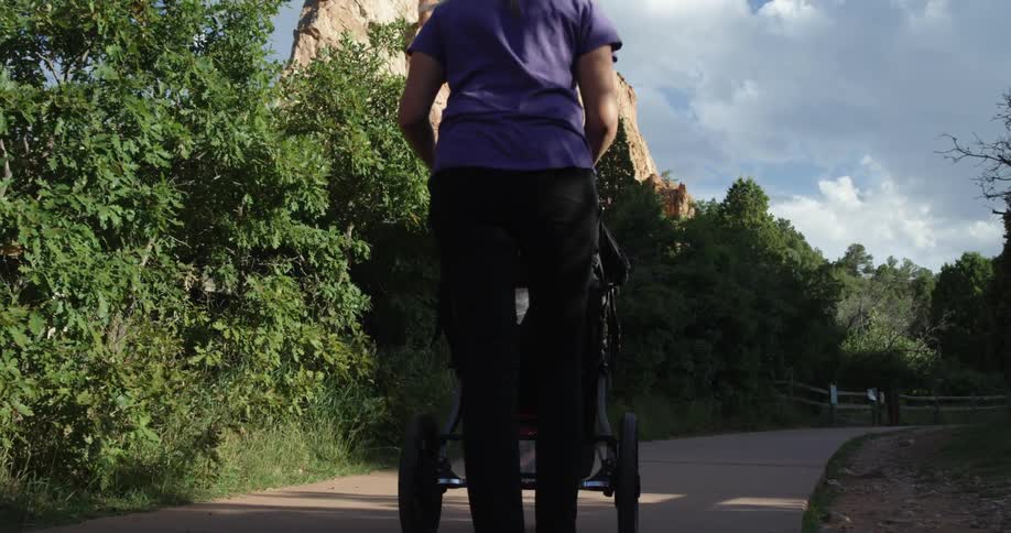 A woman pushes a stroller down a path lined by trees and shrubs