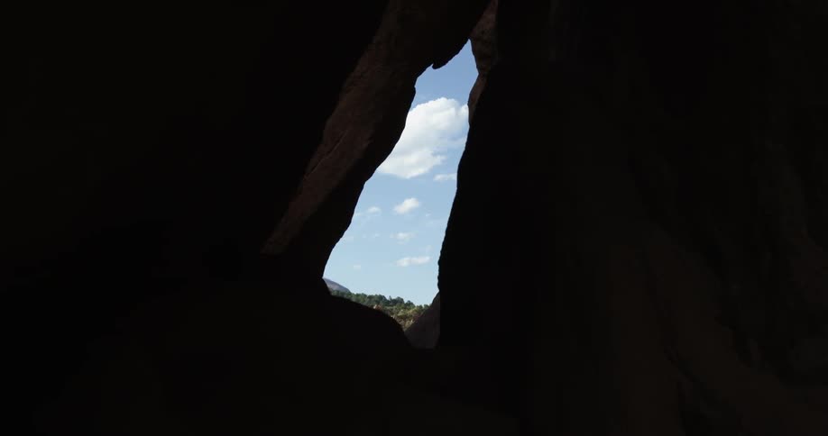 A partly cloudy day is seen from the narrow opening of a dark cave