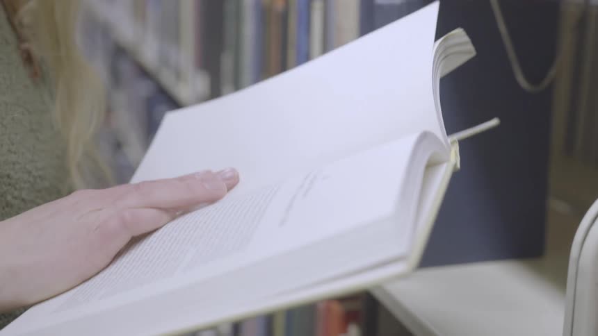 Woman reading a book from book shelf at the library
