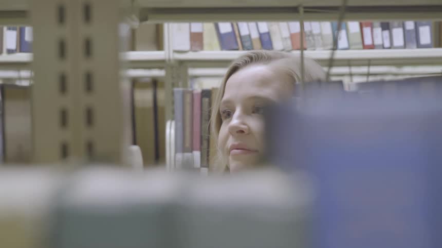 Blonde teenage girl searches for a book in the library