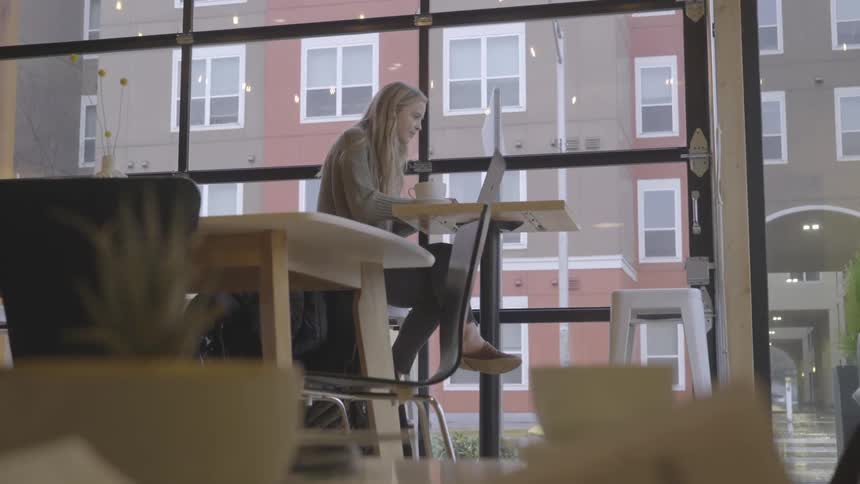 A female caucasian sitting at a table typing on a laptop