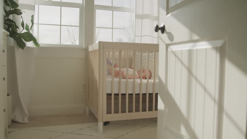 Infant moves its legs as it lays on its back in a crib