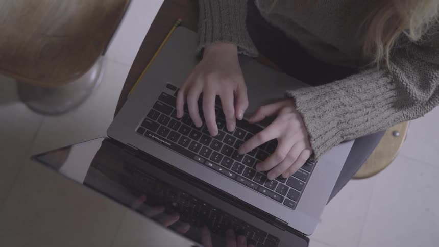 Blonde woman sitting on wooden chair with laptop in her lap touch types