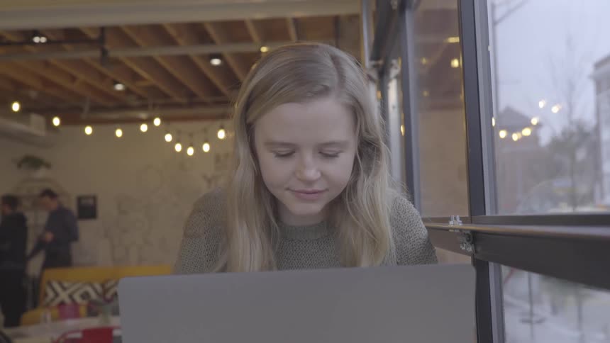 Young blonde woman working on a laptop in a cafe