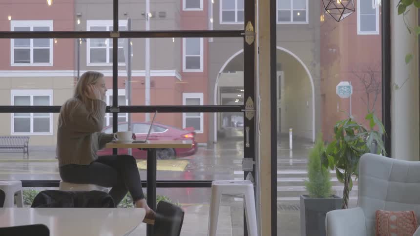 Woman sips a hot beverage while sitting in a cafe and using a laptop