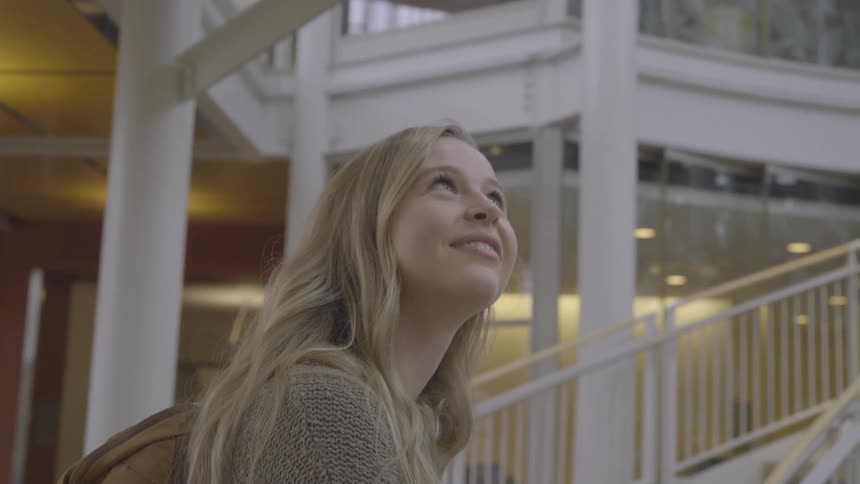 A young woman smiles as she gazes around a building while standing at the bottom of a spiral staircase