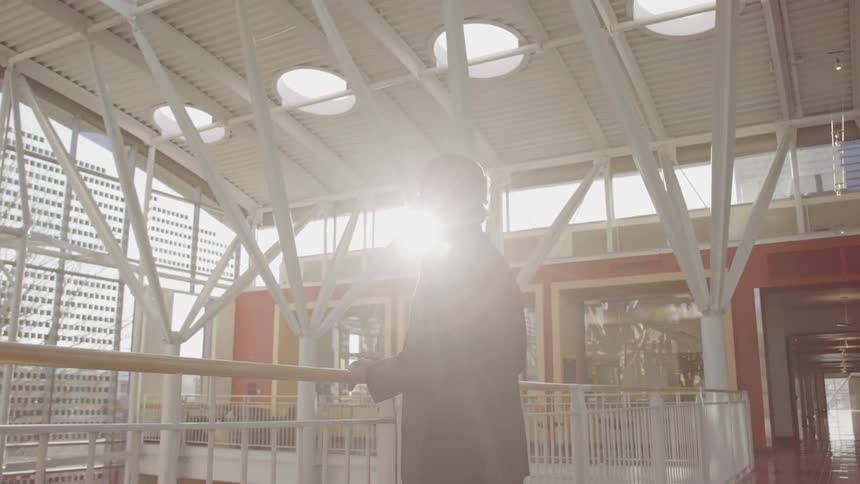 Man wearing suit stands holding banister as suns glare briefly cast him into a silhouette