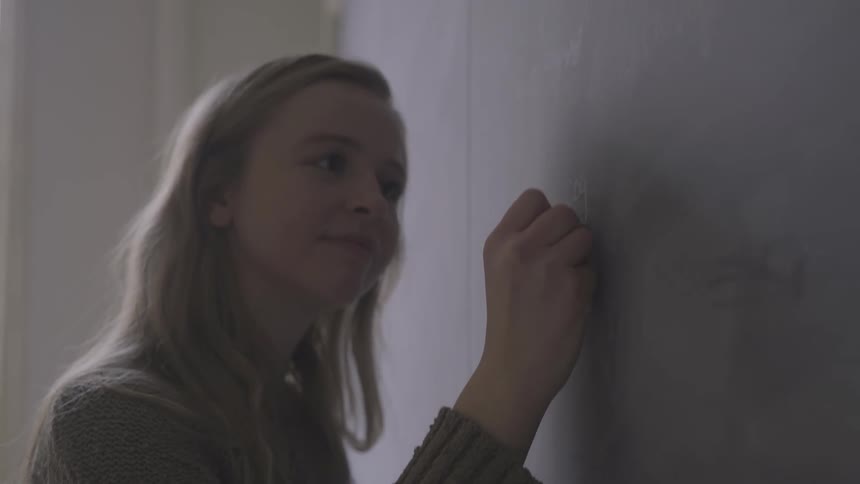 A young girl writes on a blackboard at school