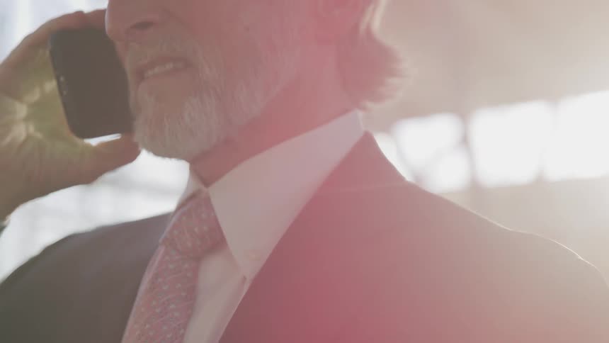 Businessman with a grey beard and a suit talks on the smartphone