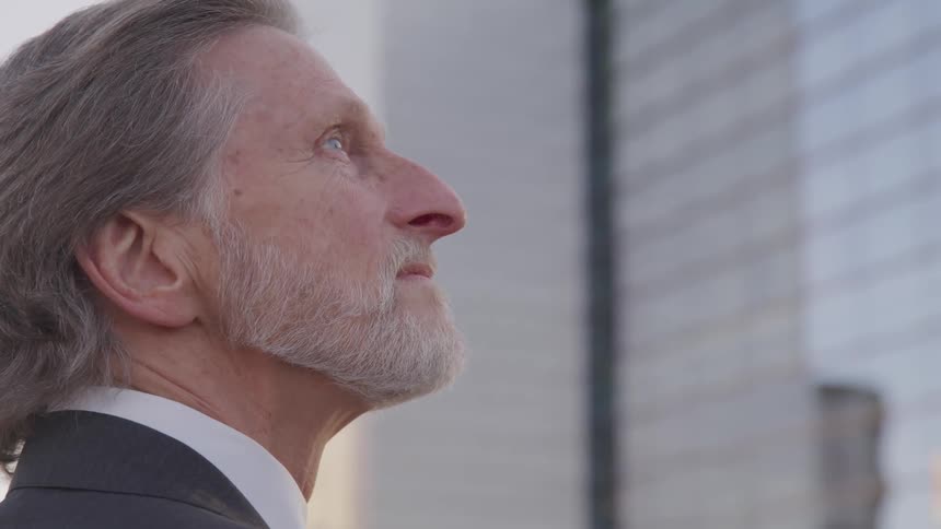 A man in a business suit stands outside and looks up at skyscrapers nearby