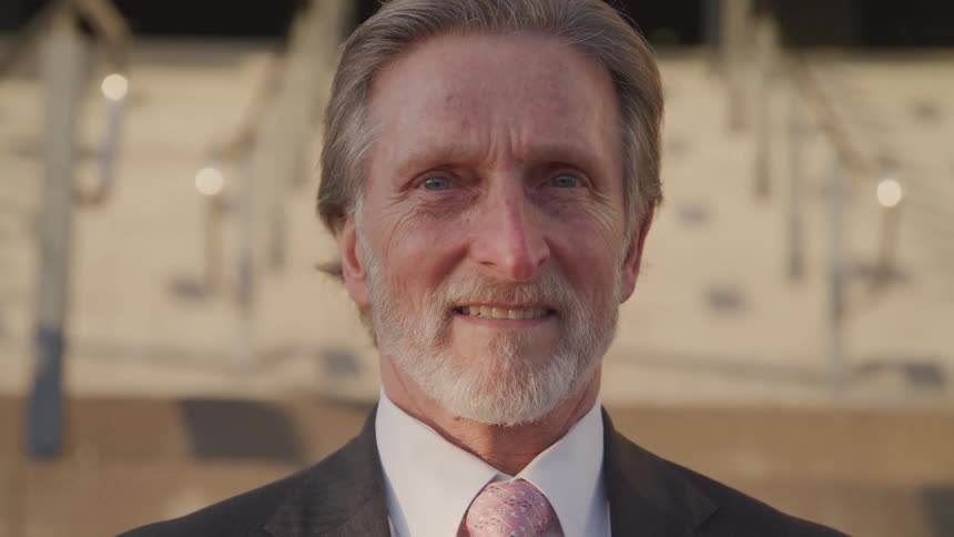 A man is smiling outside on a sunny day
