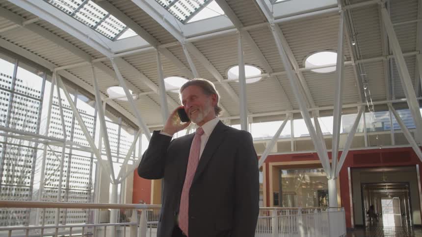 A man talks on the phone and laughs while standing in an airport atrium