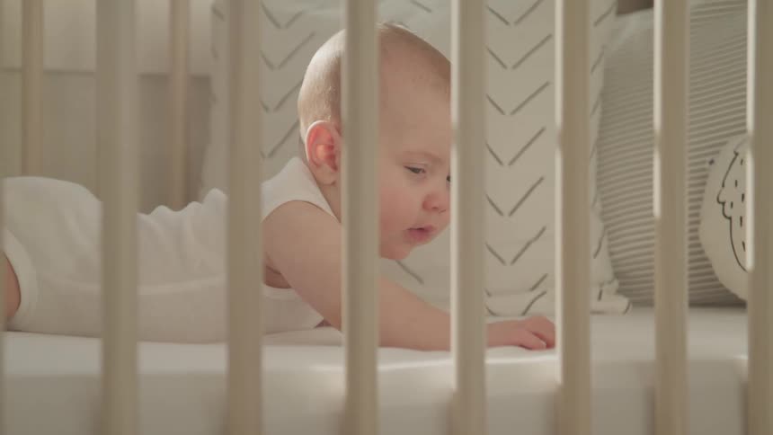 A small infant lays on its stomach in a crib with decor pillows