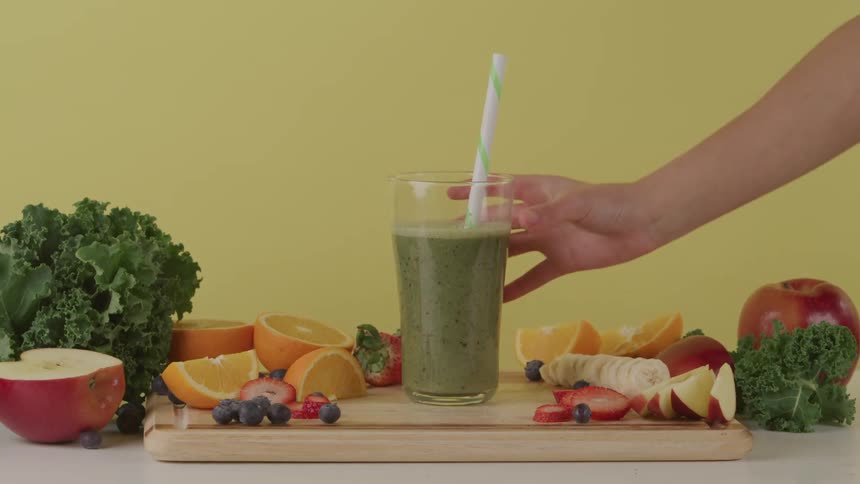 A person places a straw and picks up a glass of juice made of vegetables and fruit