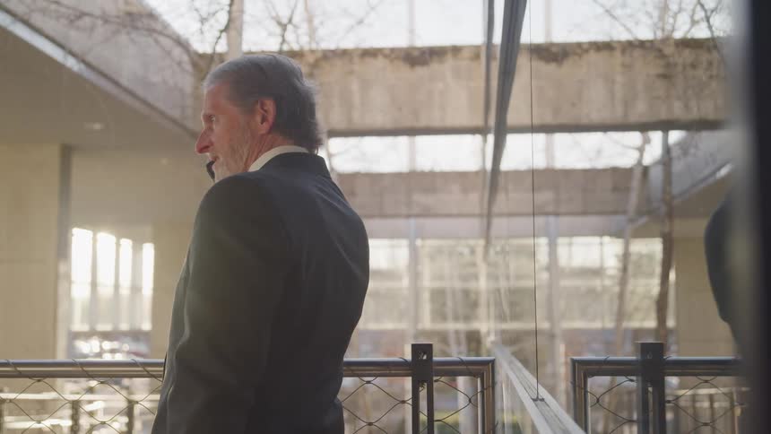 A man in an office building stands and talks on a cell phone