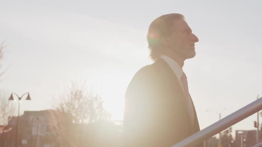 Man wearing a suit climbs up the stairs of a building at sunset