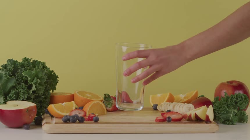 Womans hand puts a glass on a cutting board with sliced fruits on it