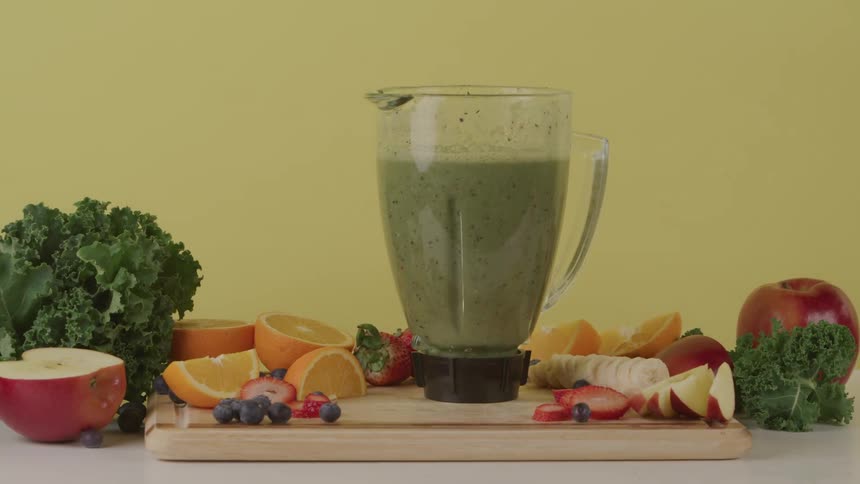 A woman sets a blender filled with smoothie down beside cut fruit