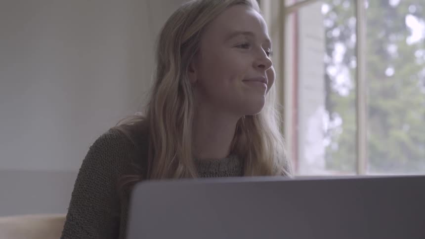 Young blonde teenager works happily on a laptop at home