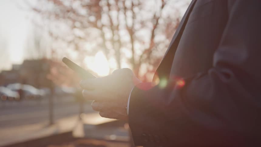 A man in a suit uses a smartphone while standing outdoors during the day