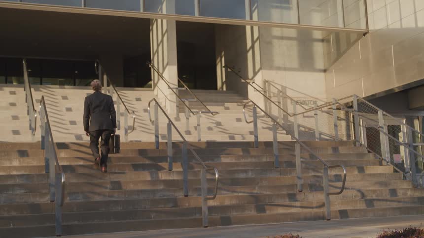 Businessman wearing a suit and carrying a briefcase goes up the stairs to the building