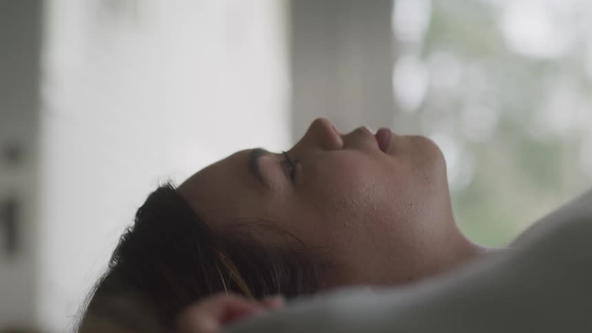 A young woman slowly opens her eyes as she lies motionlessly in a house during the day