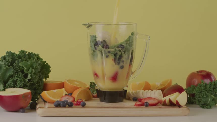 Fruits and vegetables being added to a blender is displayed