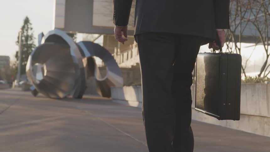 Man carrying briefcase walks along front of building toward statue